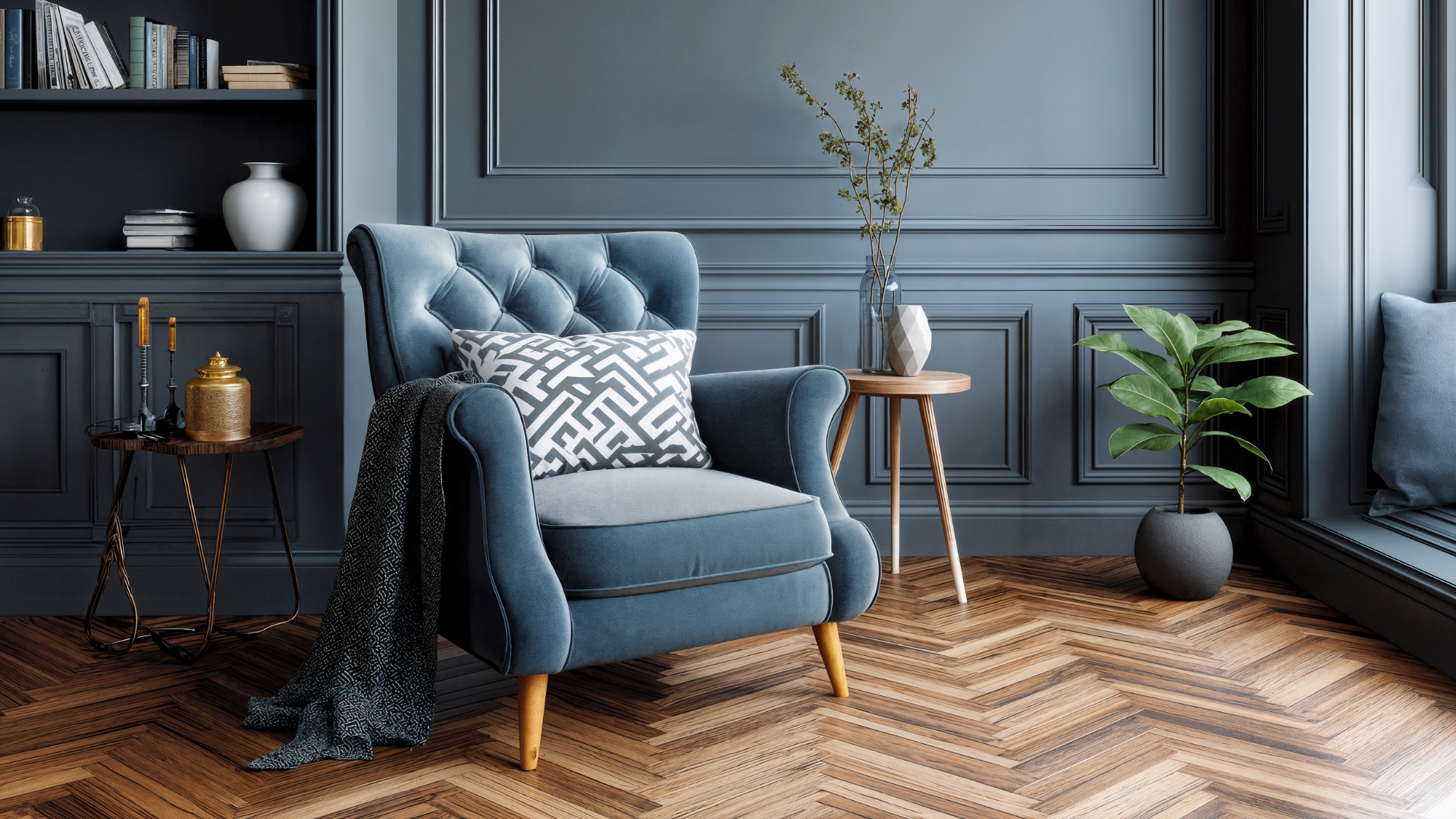Blue tufted armchair with patterned pillow in a dark paneled living room, with plants and a chevron wood floor.