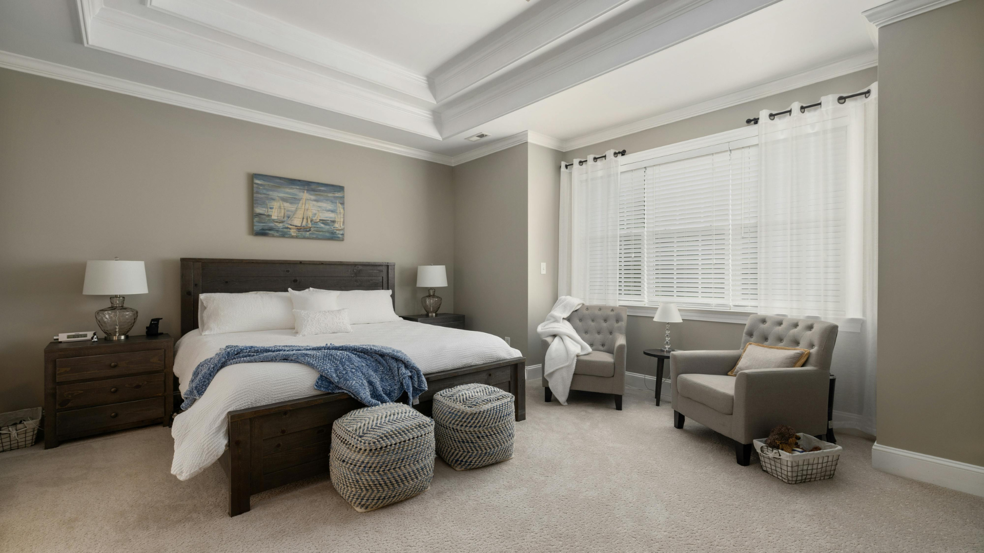 Bright bedroom with a bed, gray chairs, window seat, and beige carpet under soft natural light