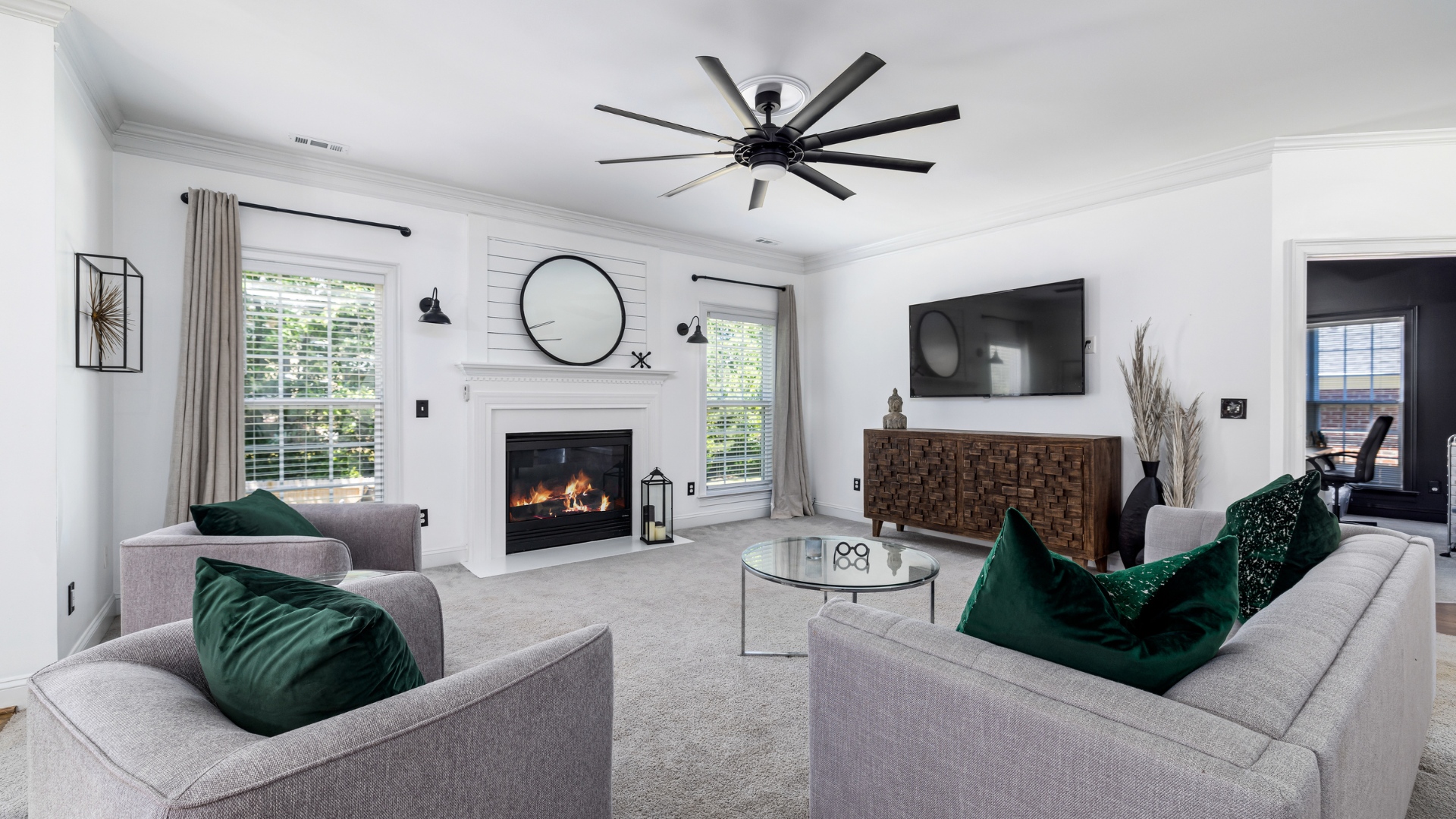 Bright living room with gray sofas, fireplace, large wall clock, TV, and ceiling fan