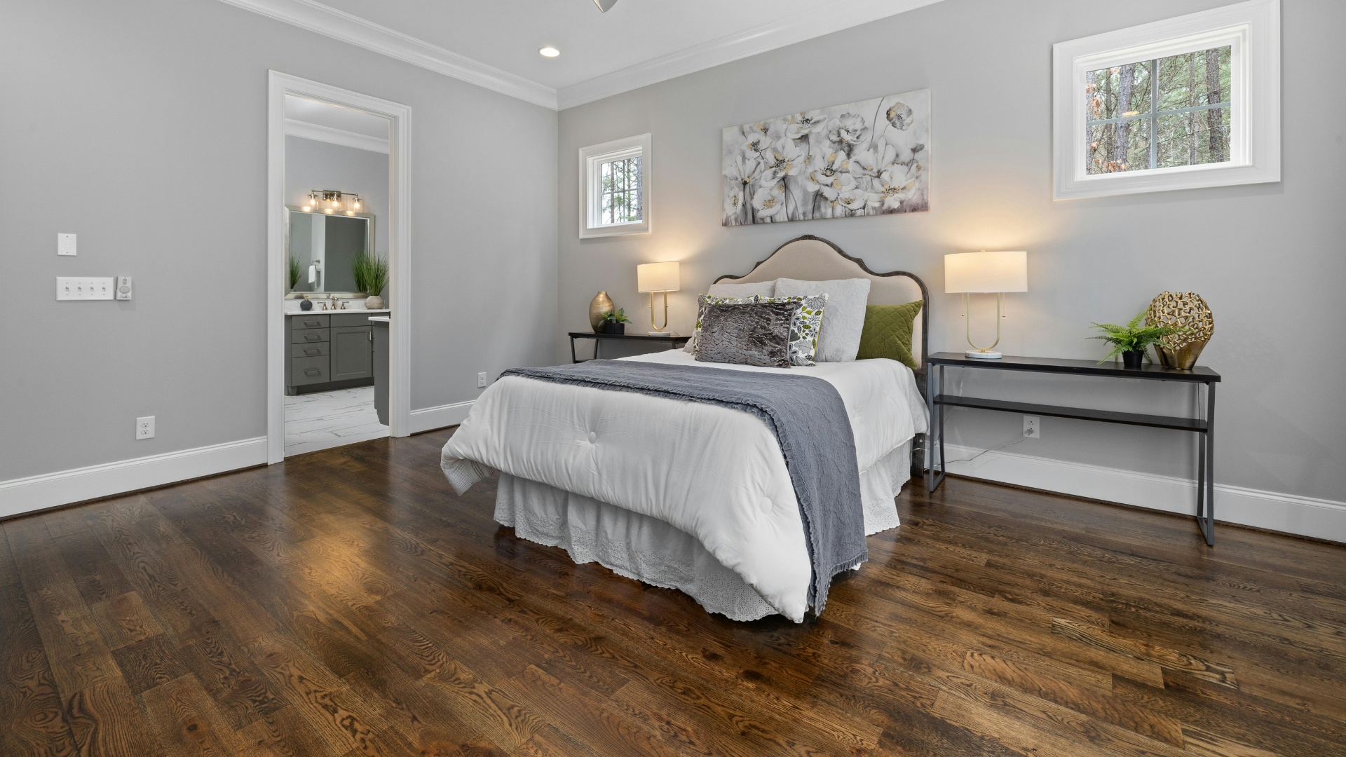 Modern gray bedroom with a large bed, wood floors, and a console table beneath two windows.