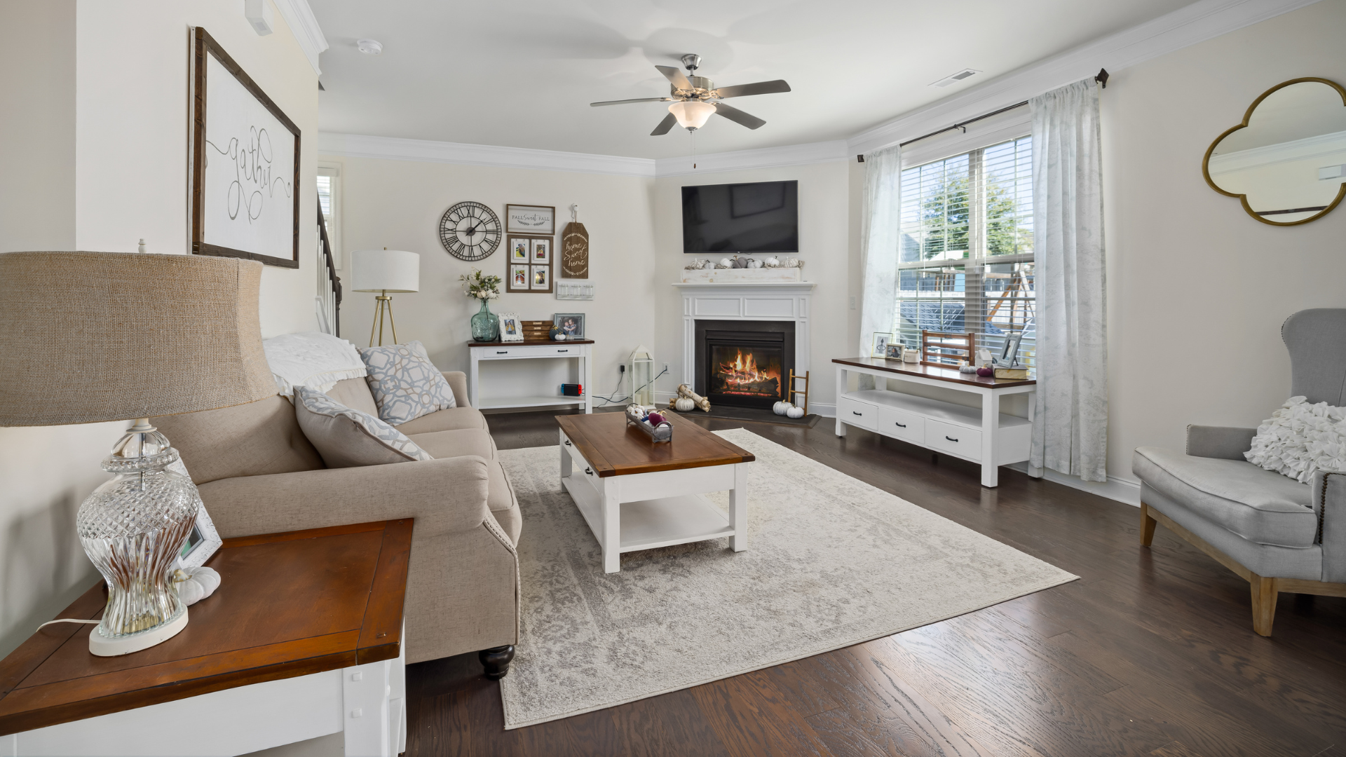 Bright living room with beige sofa, fireplace, wall TV, and large window with white curtains