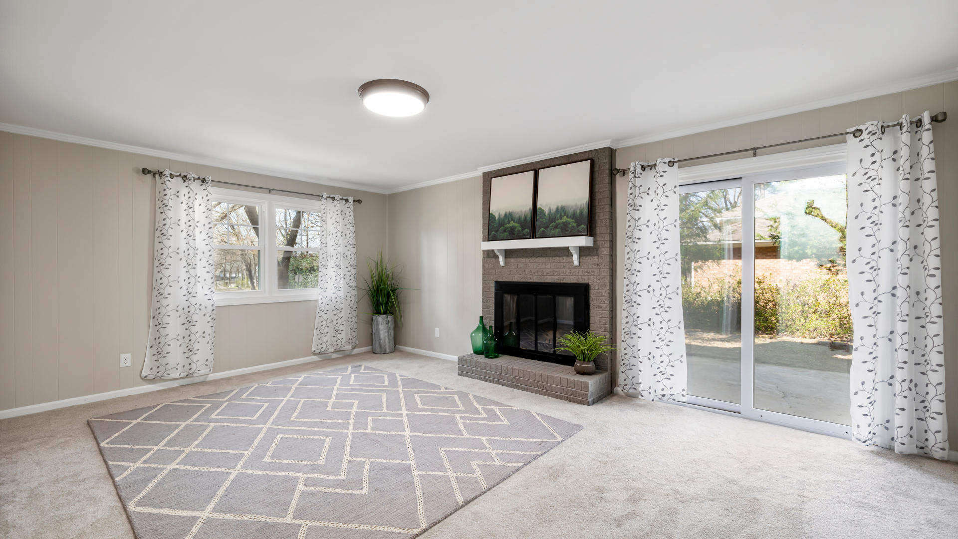 Bright living room with a fireplace, large windows, light carpet, and a patterned rug