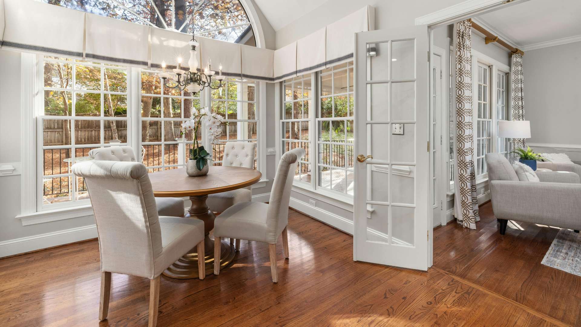 Bright sunroom dining area with white chairs, round table, French doors, and hardwood floors