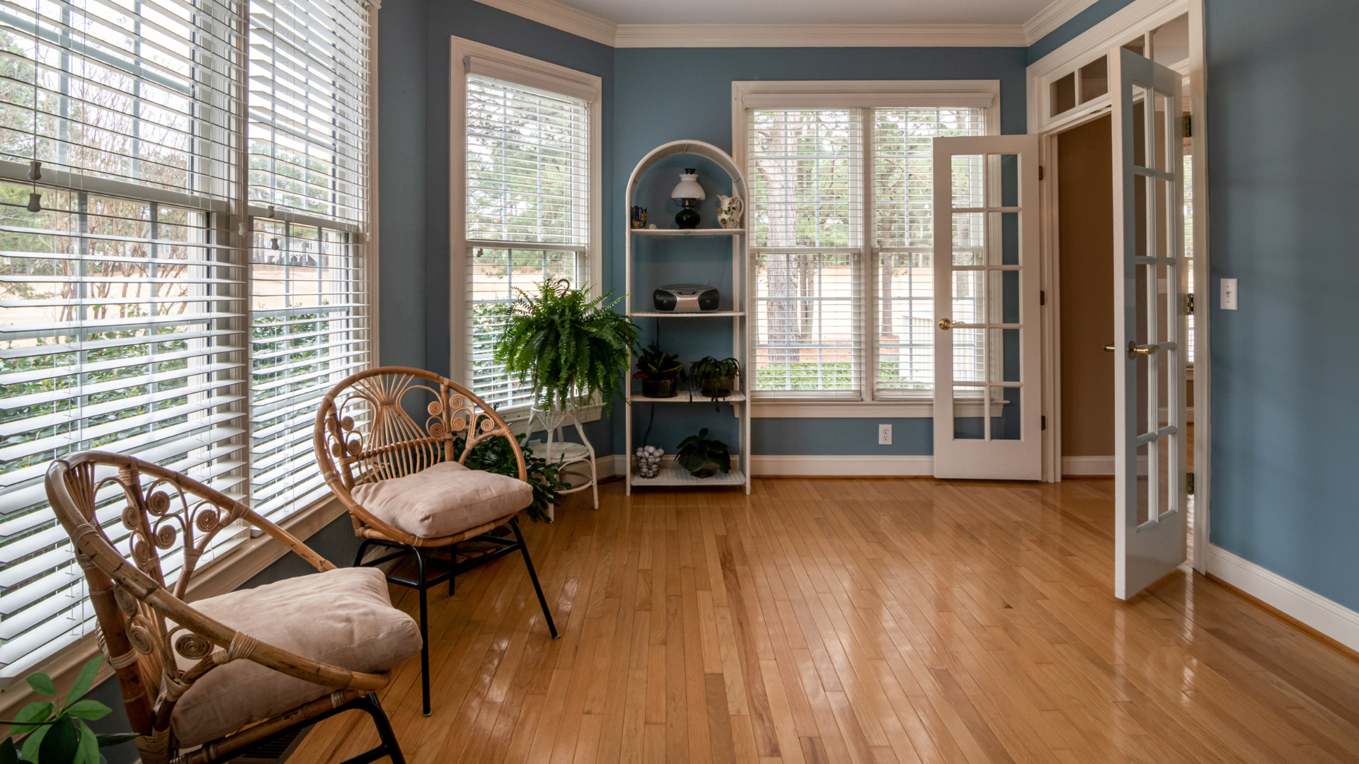 Bright sunroom with wicker chairs, blue walls, hardwood floor, and large windows with blinds