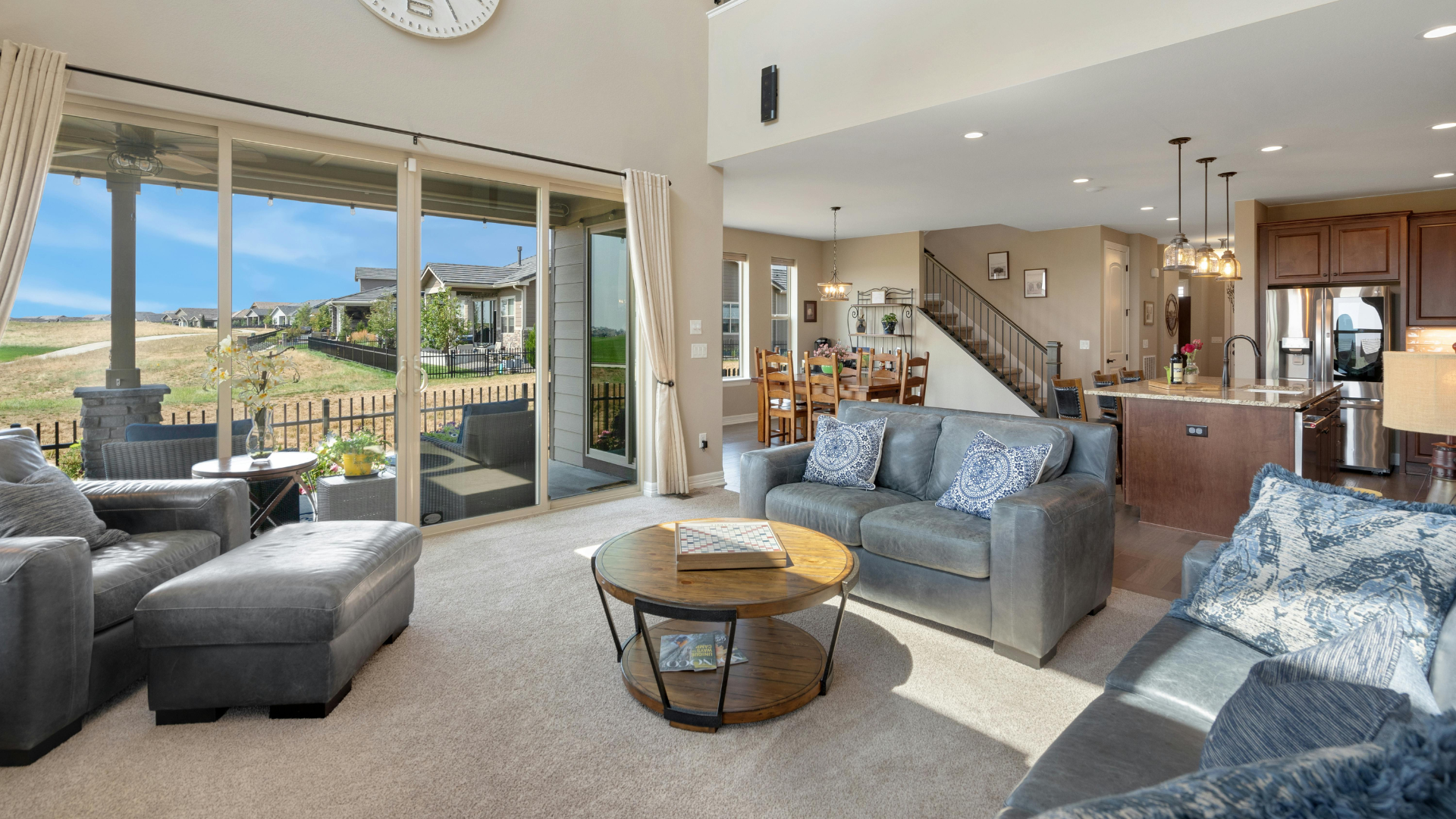 Bright open living room with gray sofas, coffee table, and large sliding doors to a sunny deck and hills.