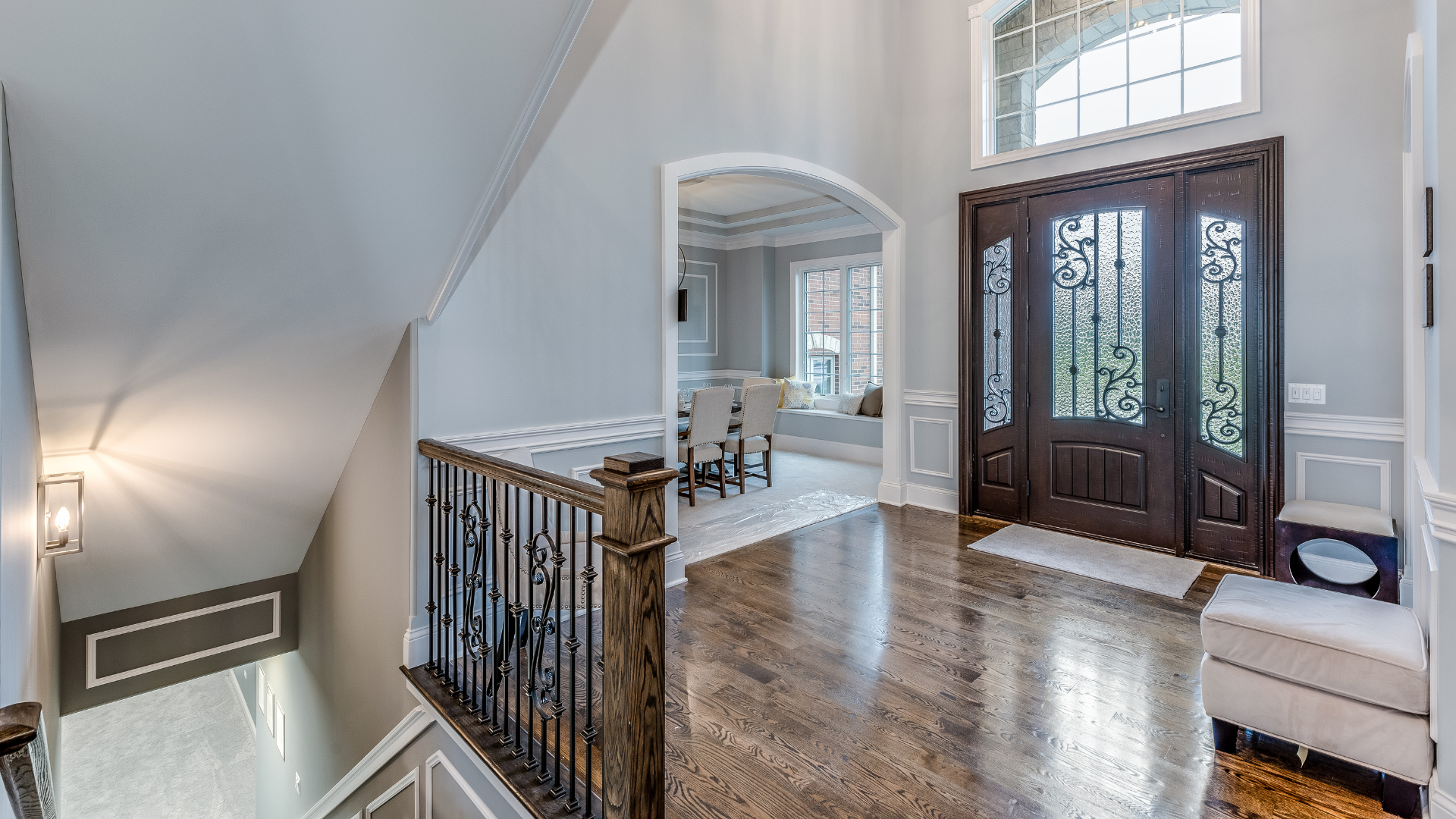 Bright foyer with hardwood floors, double front doors, staircase railing, and arched opening to a dining room.