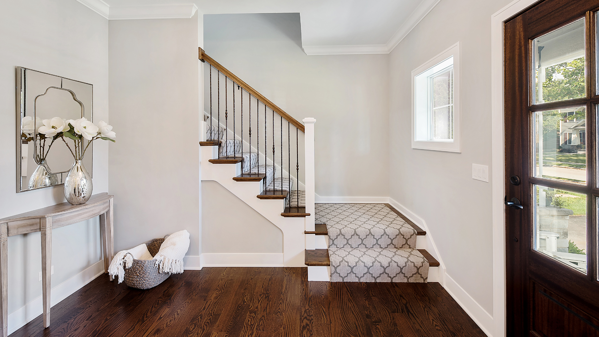 Bright foyer with staircase, dark wood floors, console table, and glass front door