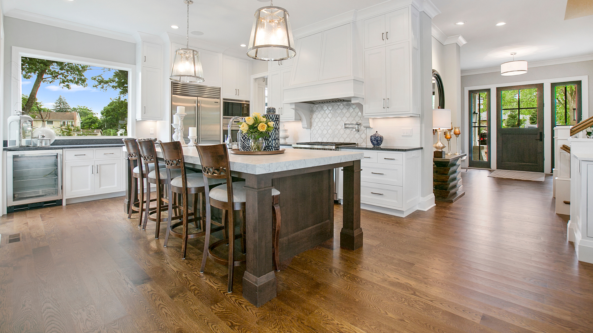 Bright white kitchen with island, wooden stools, hardwood floors, and a view of a patio door and backyard.