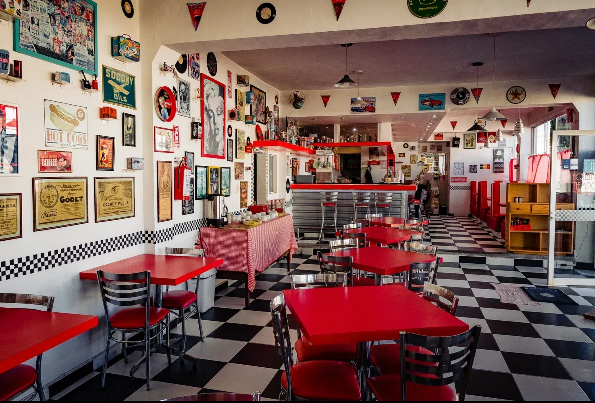 Interior de estilo retro con mesas rojas, suelo de baldosas blancas y negras y decoración vintage.