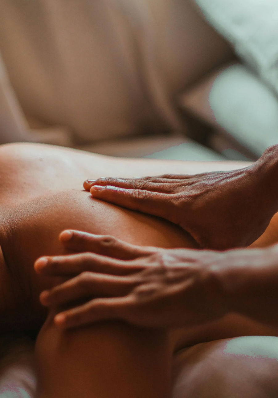 Manos masajeando la espalda desnuda de una persona en un ambiente de spa con tonos cálidos.