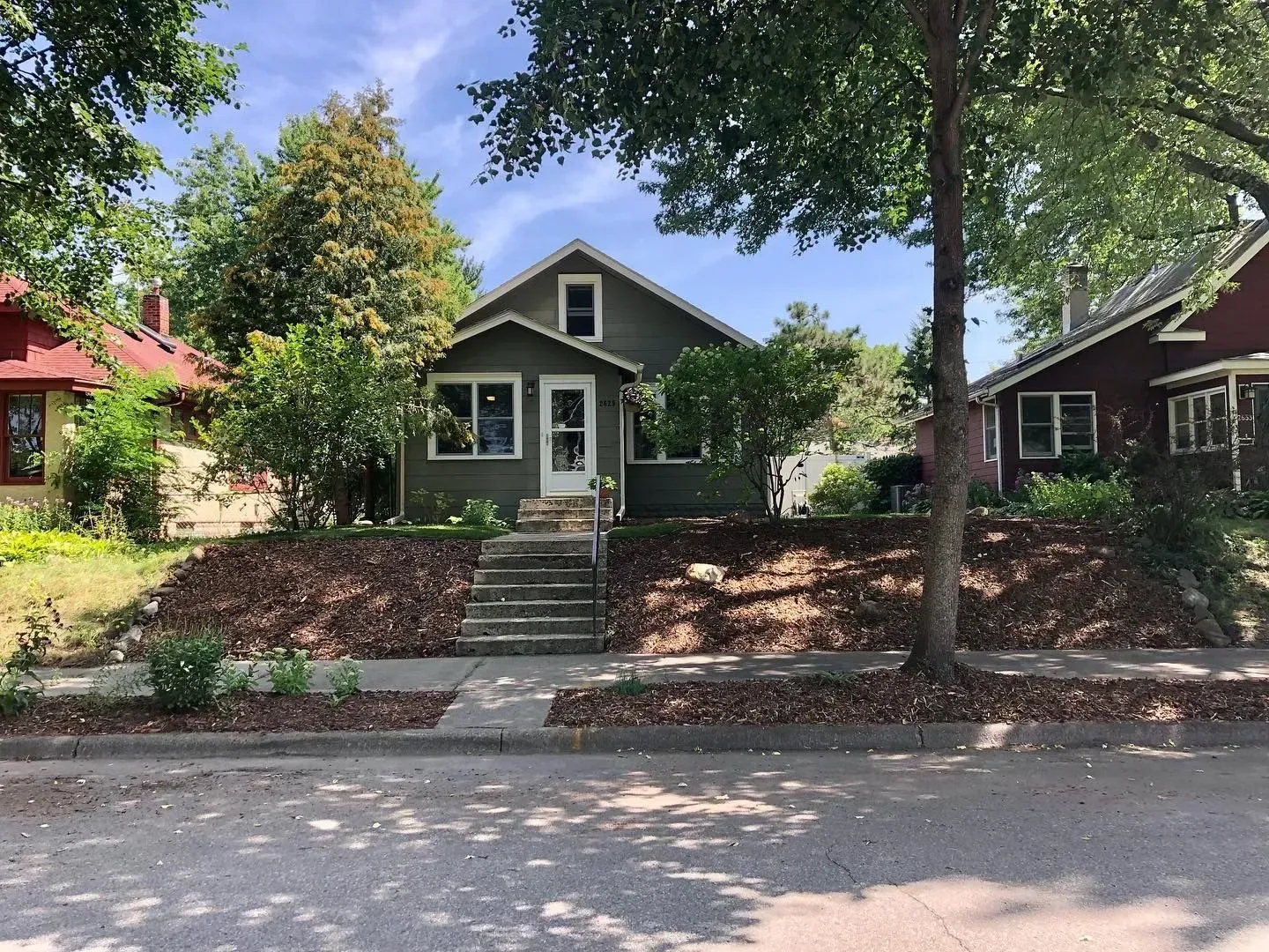 A green house with steps leading to the front door, set on a slight hill with a sidewalk in front.