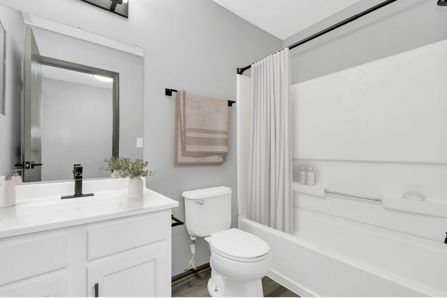 Bright white bathroom with vanity, toilet, tub-shower, and beige towel.