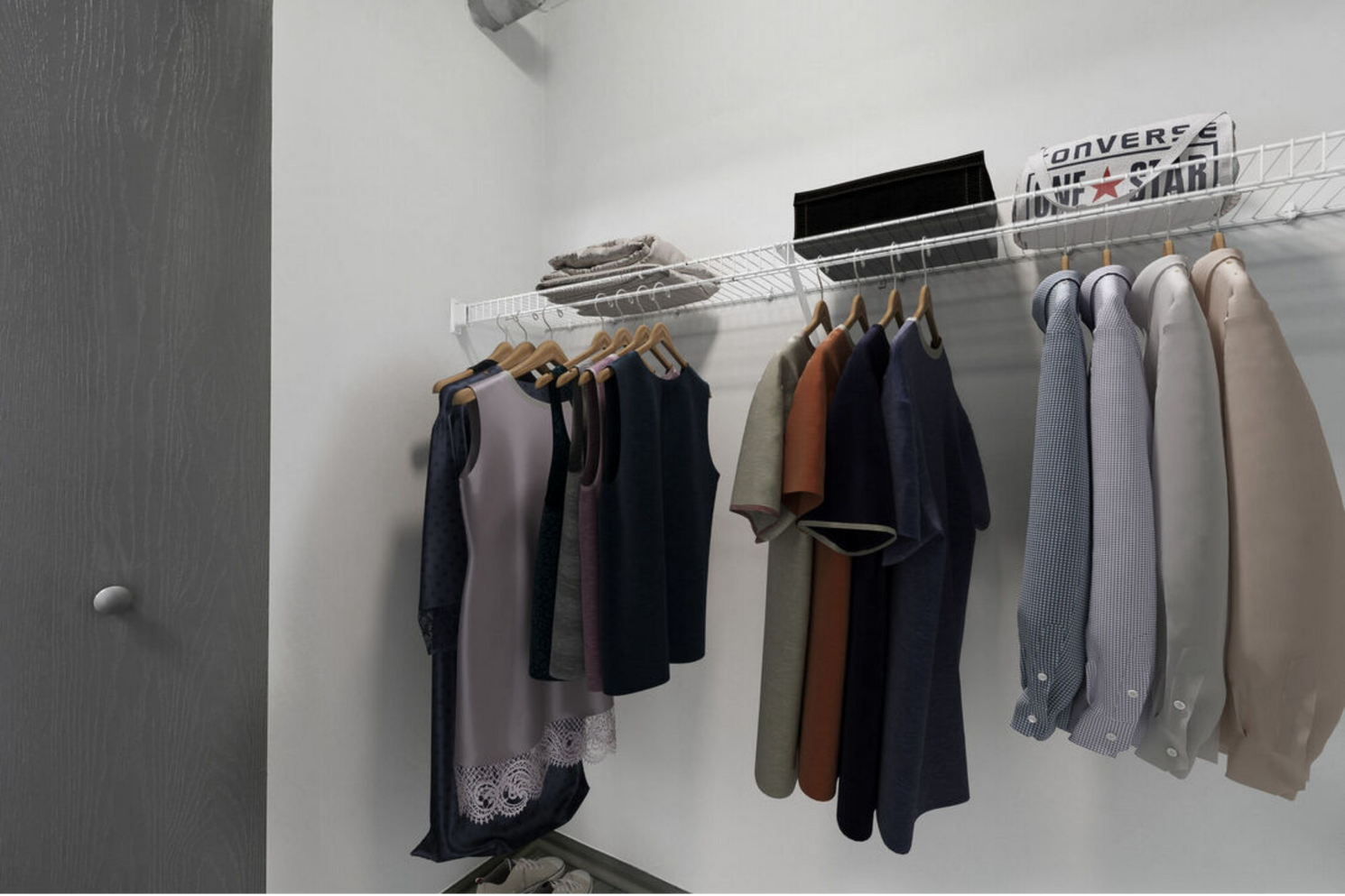 Closet with hanging clothes on a wall rack beside a gray door and folded items on top shelves