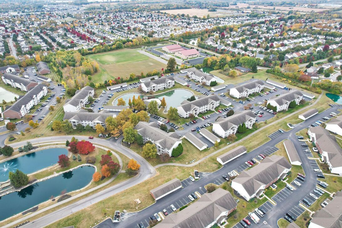 Aerial view of a suburban neighborhood with houses, streets, ponds, and green fields