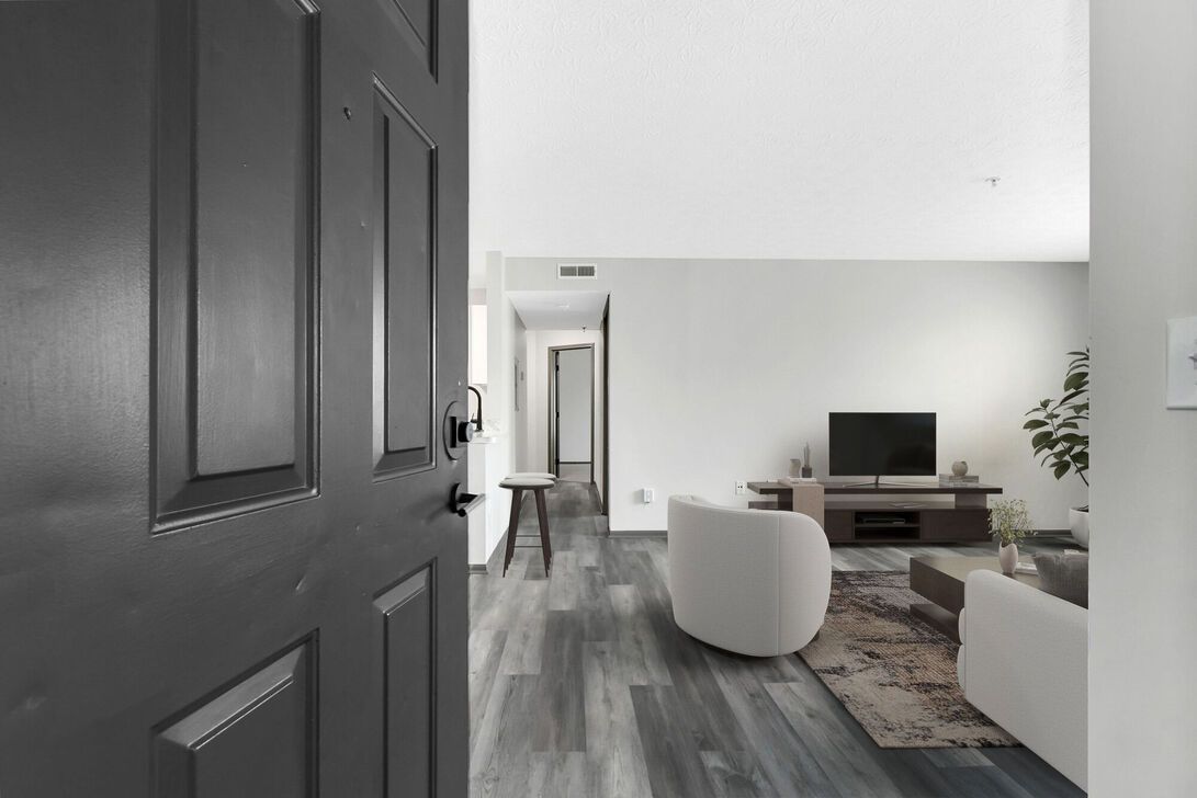 View through a black door into a bright modern living room with gray floors, white furniture, and a TV.