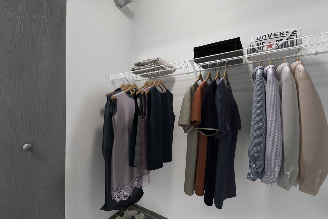 Open closet with hanging shirts and sweaters on a white clothes rack