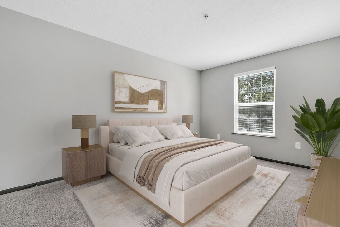 Bright bedroom with a neatly made bed, nightstand, window, rug, and potted plant in a neutral color palette