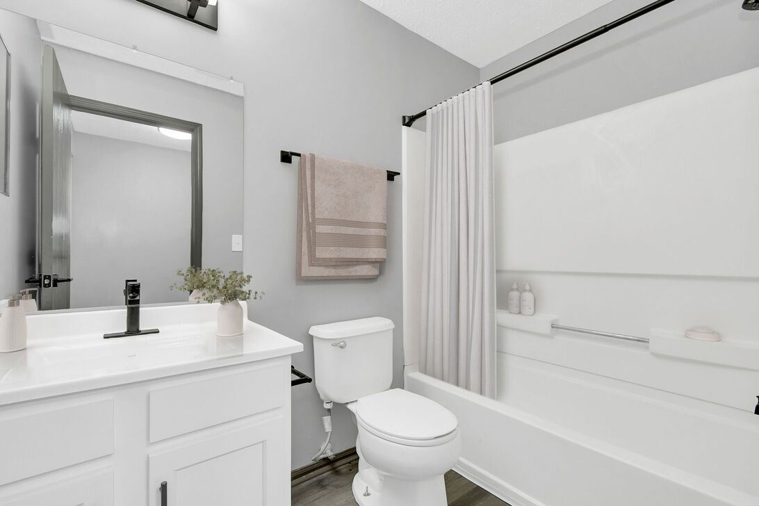 Bright white bathroom with sink, toilet, bathtub, shower curtain, and beige towels