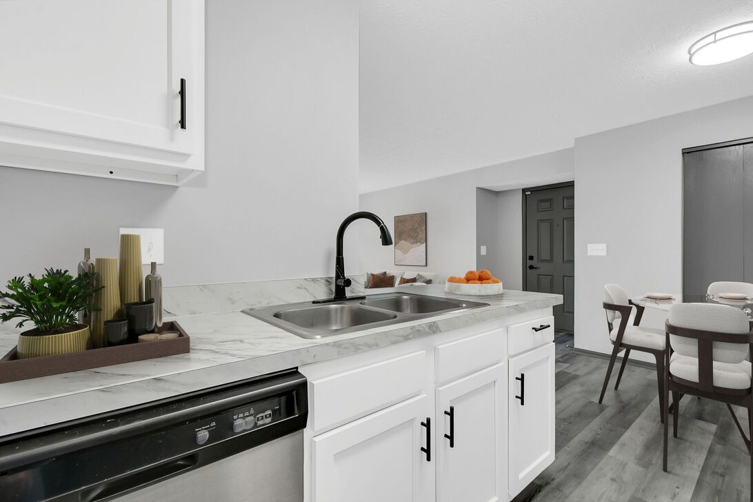 Bright white kitchen with black fixtures, stainless sink, and small dining area by the window