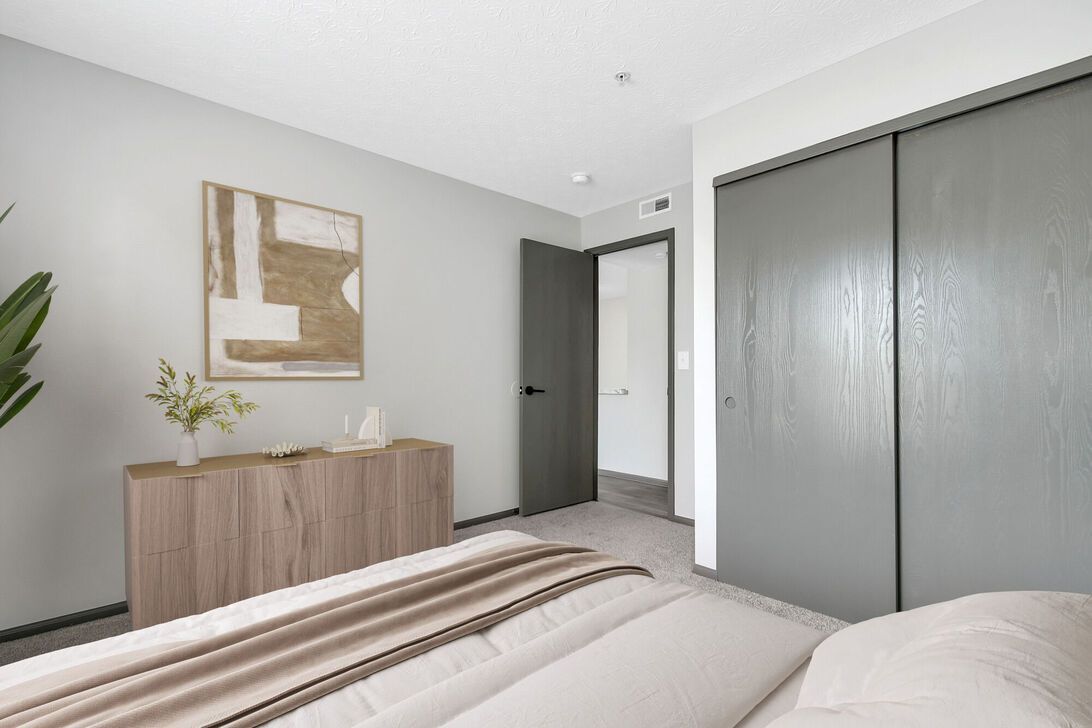 Modern bedroom with a bed, wooden dresser, wall art, and sliding closet doors