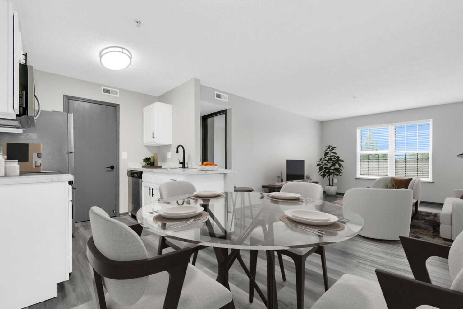Bright modern apartment living area with a dining table, white kitchen, gray sofa, and window seat.