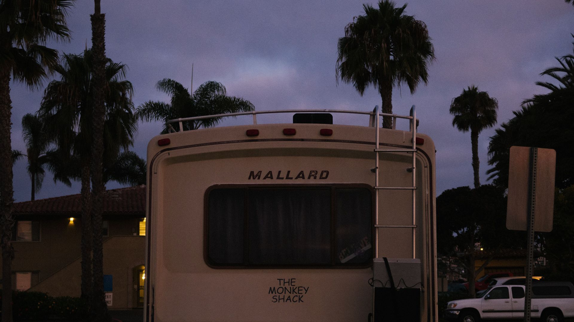 Parked Mallard RV at dusk with palm trees and houses in the background.