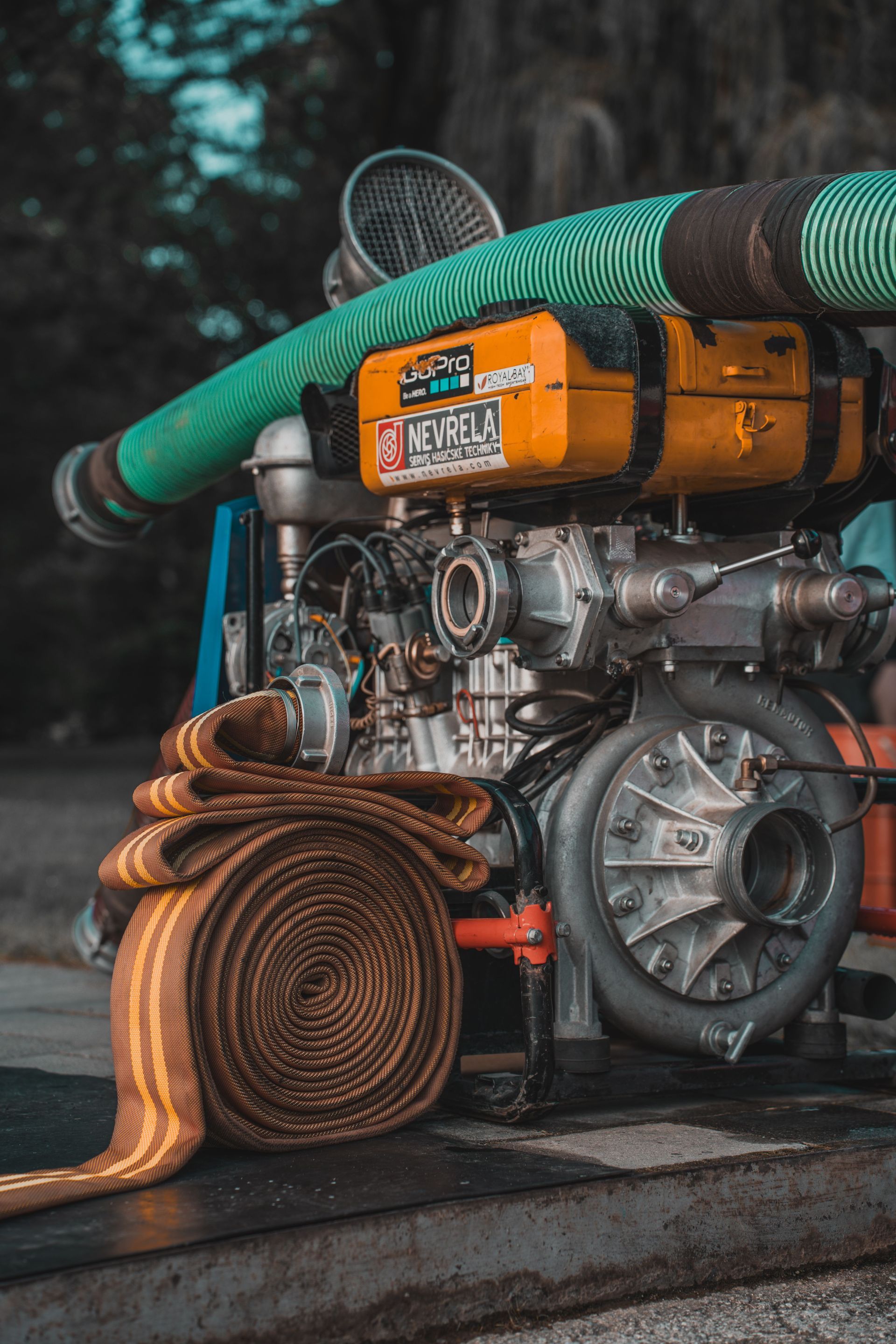 Orange industrial engine with green hose and coiled brown hose, sitting outdoors on a wooden platform.