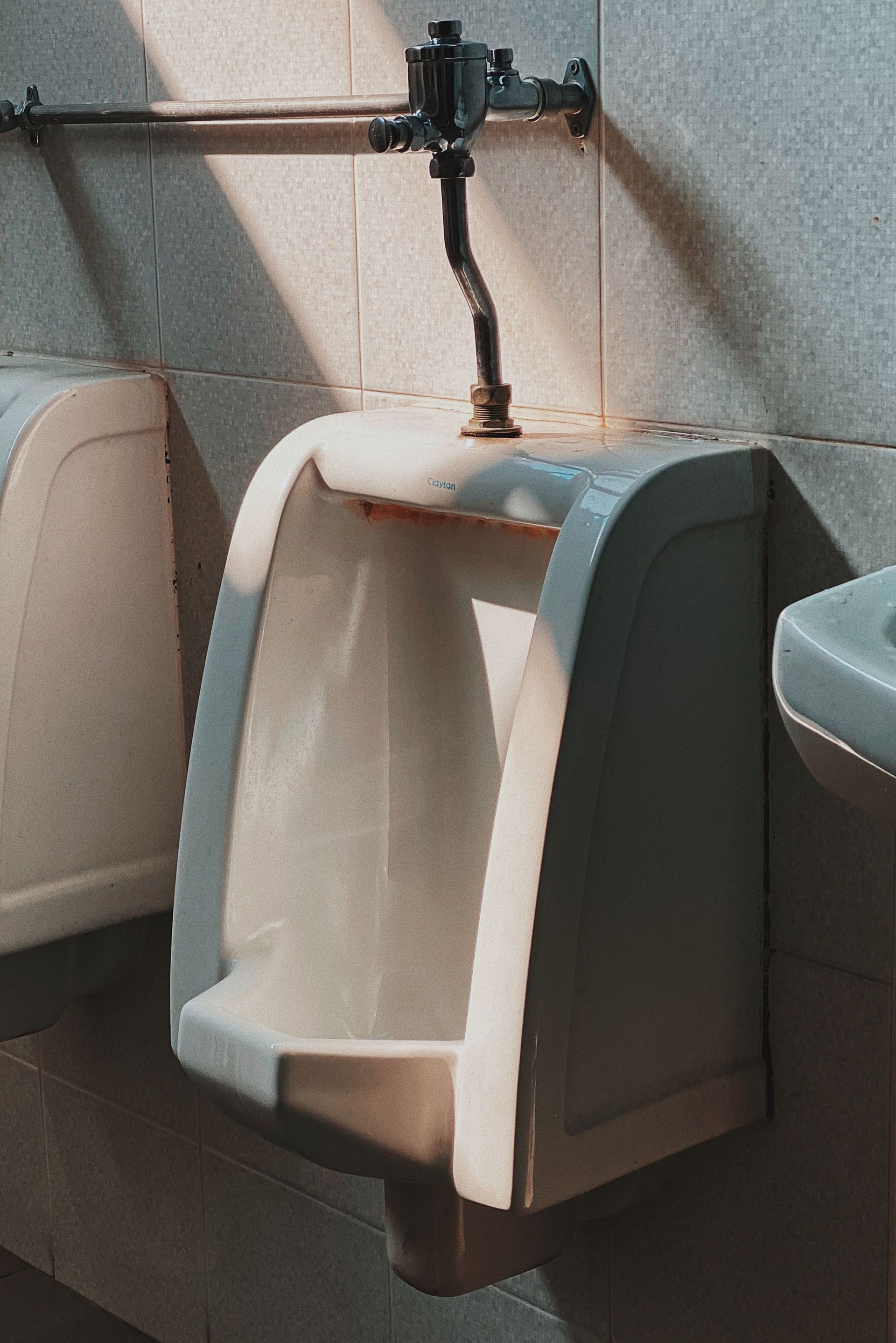 White wall-mounted urinal in a tiled restroom with a flush pipe above