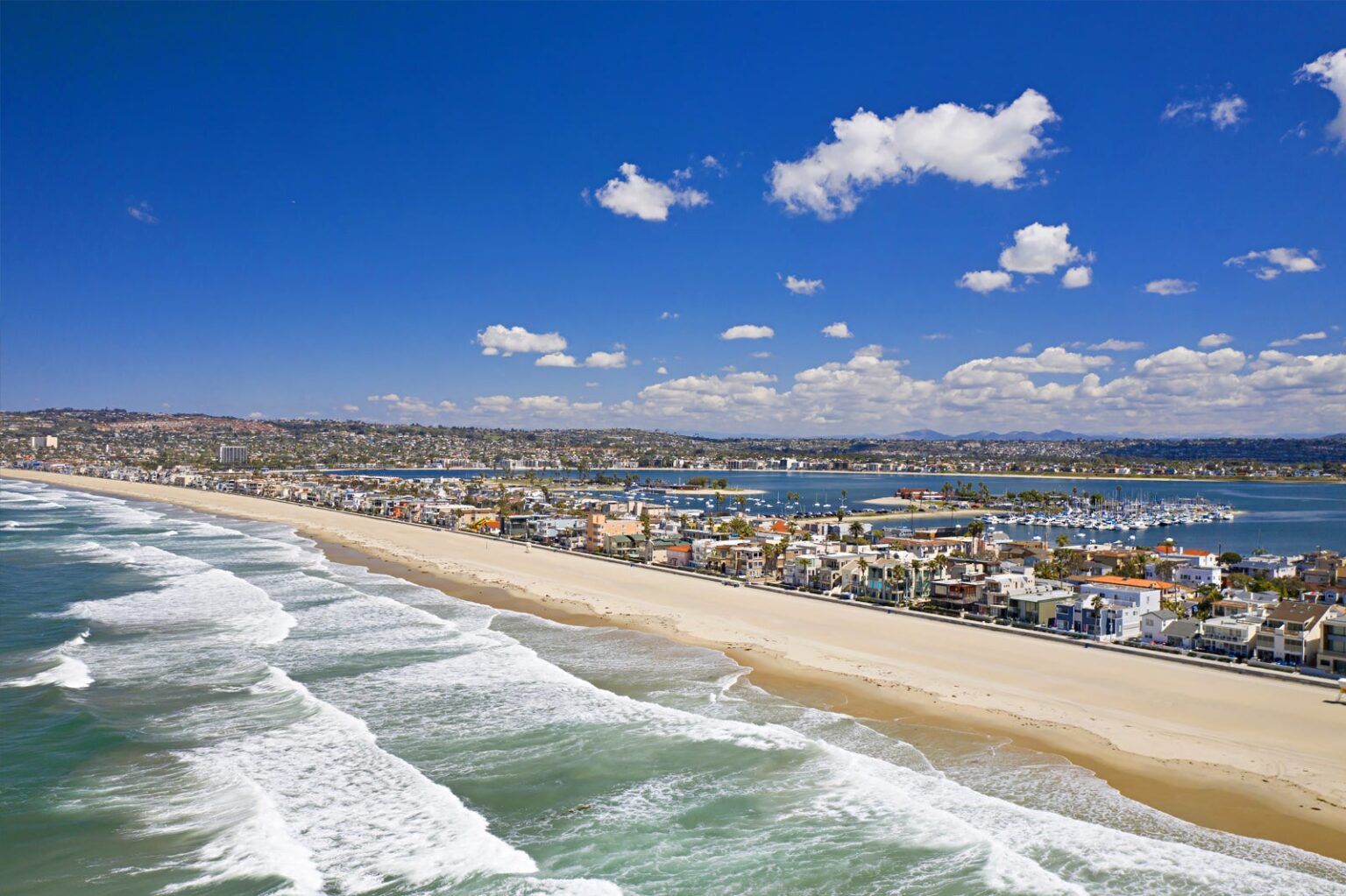 An aerial view of a beach with waves crashing on it and a city in the background.