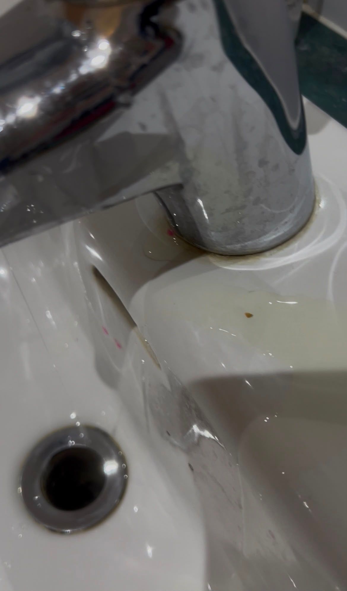 Chrome faucet over a white sink with water droplets near the drain