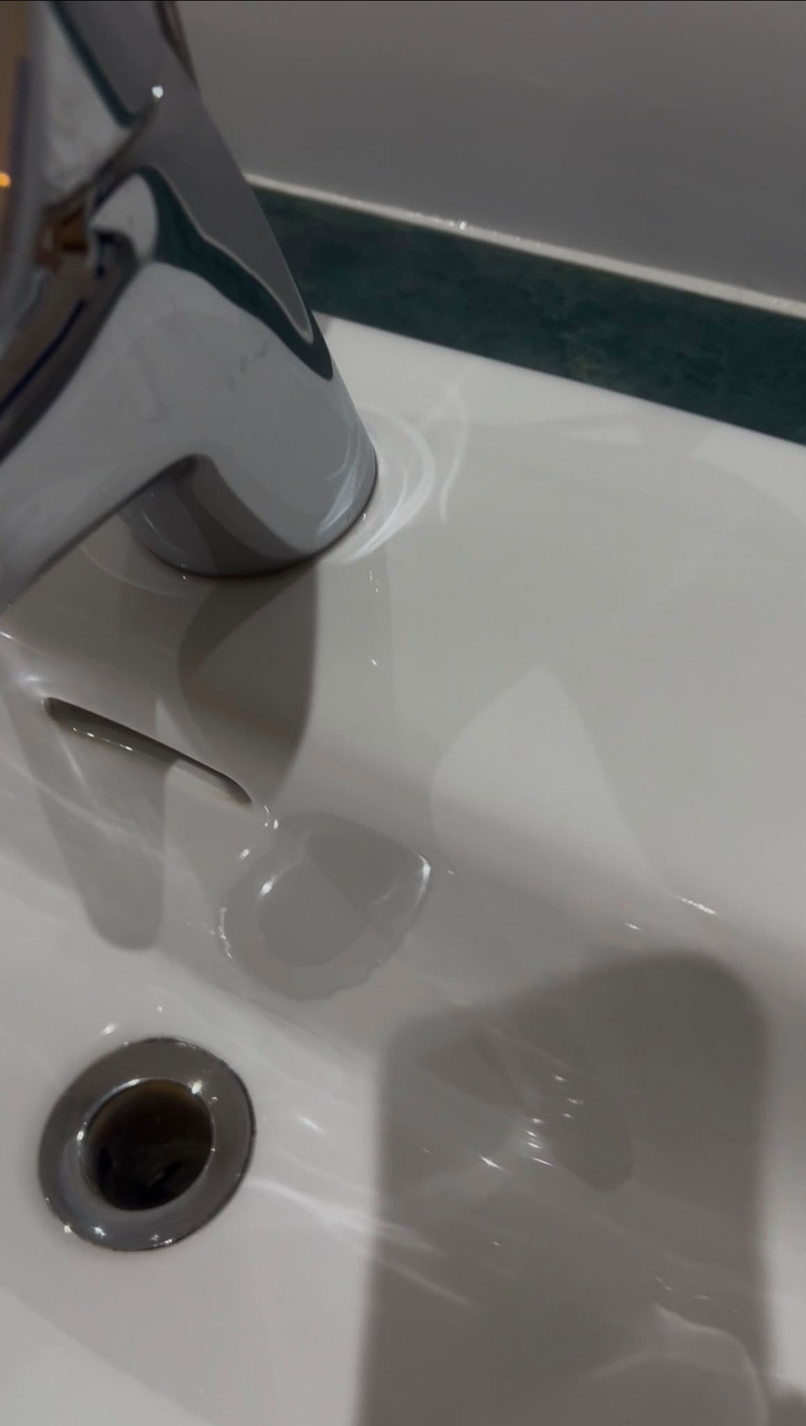 Chrome faucet over a white bathroom sink with a drain.