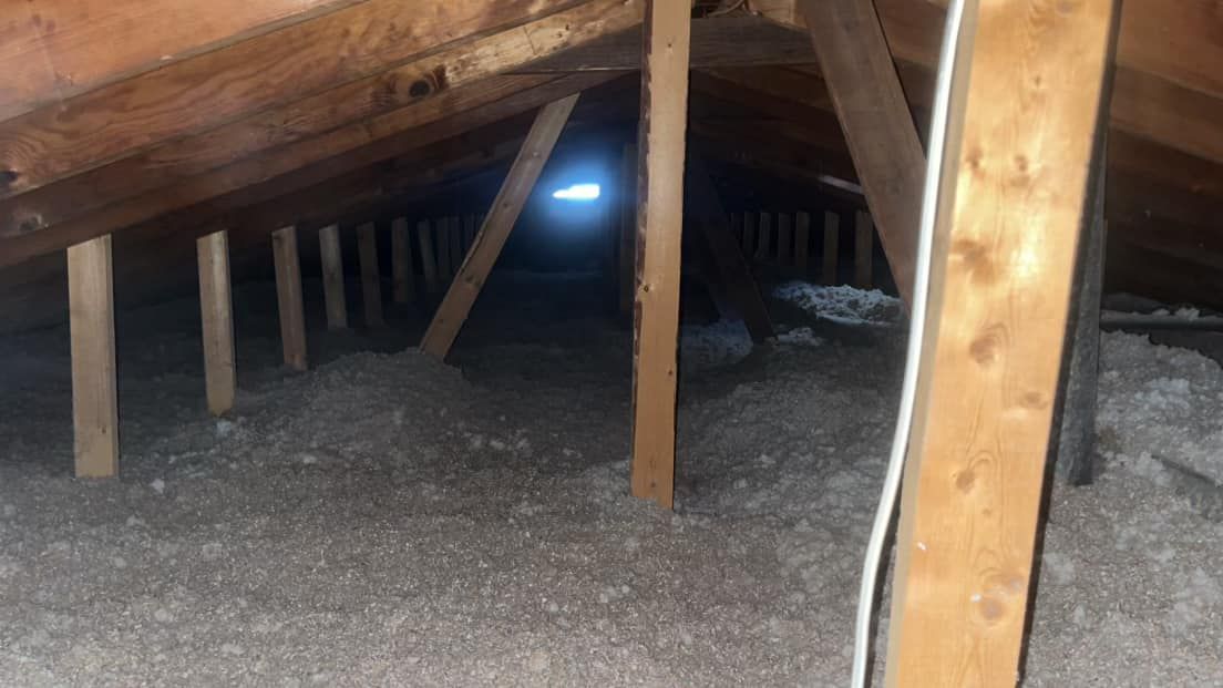 An attic interior with wooden beams and insulation. A bright light shines in the distance, indicating an opening.