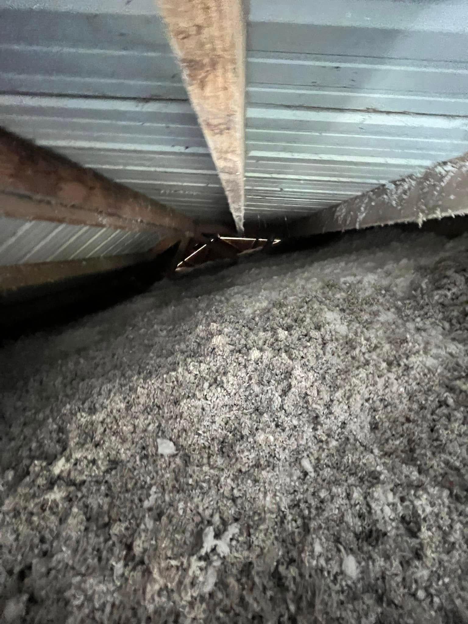 View from inside an attic, showing insulation, wooden beams, and light shining through a gap.