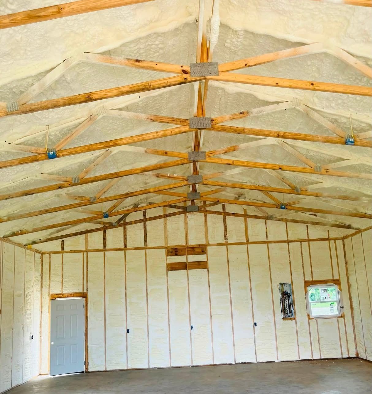 Interior of an unfinished metal-framed building with insulated roof, white wall panels, and a gray door