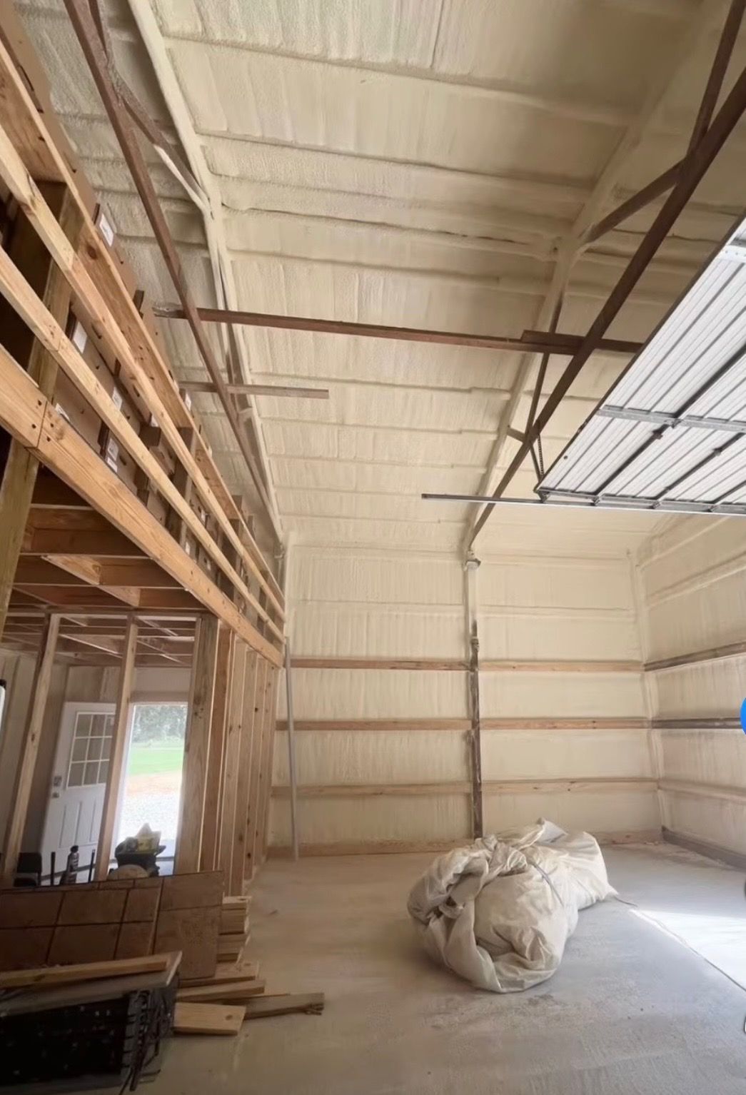 Empty industrial interior with high ceiling, exposed framing, and a large white tarp on the concrete floor.