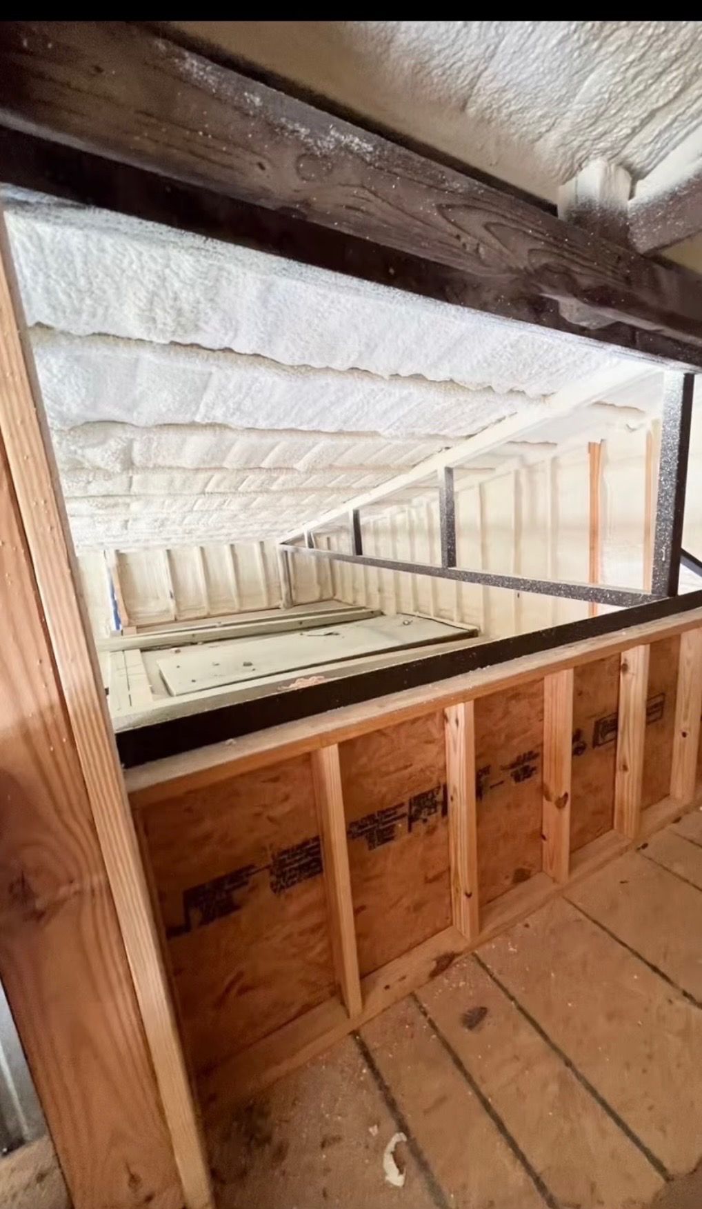 View down a loft opening with exposed wood framing and white foam insulation panels.