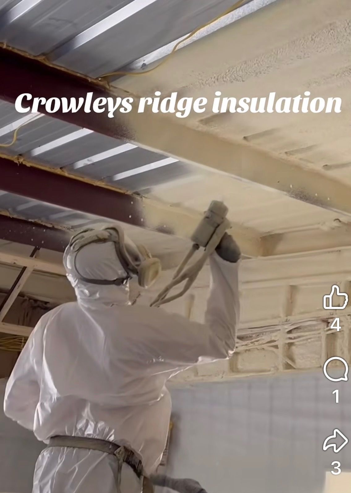 Worker spraying ridge insulation on a ceiling with exposed beams in a construction space