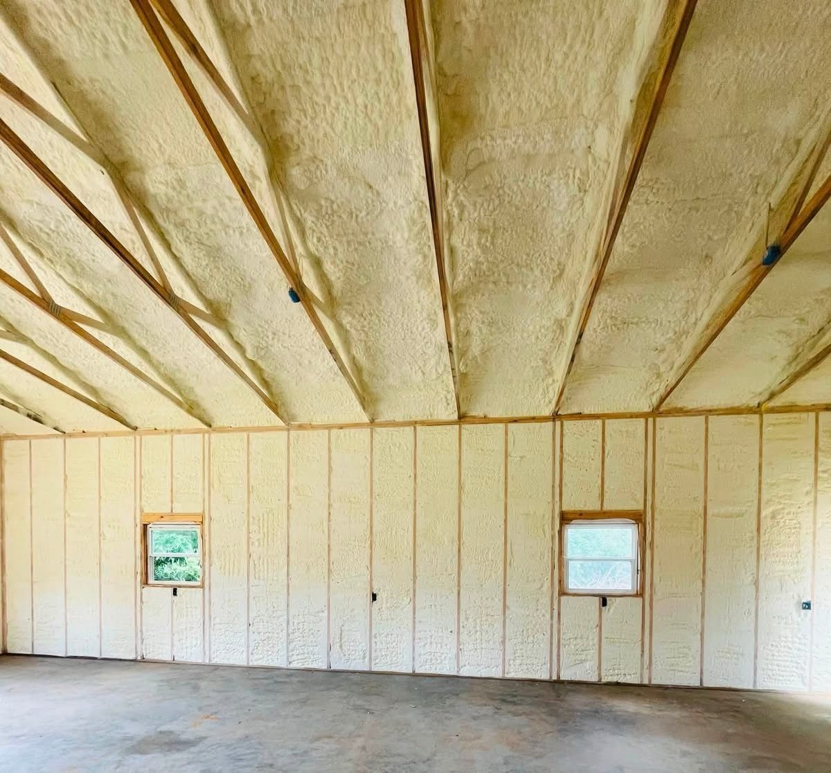 Empty insulated room with unfinished white walls, exposed ceiling beams, and two small windows.