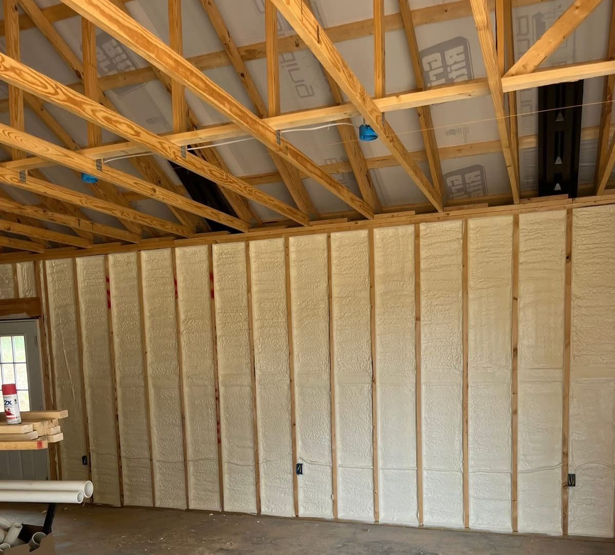 Interior of a framed building under construction with exposed roof trusses and insulated walls