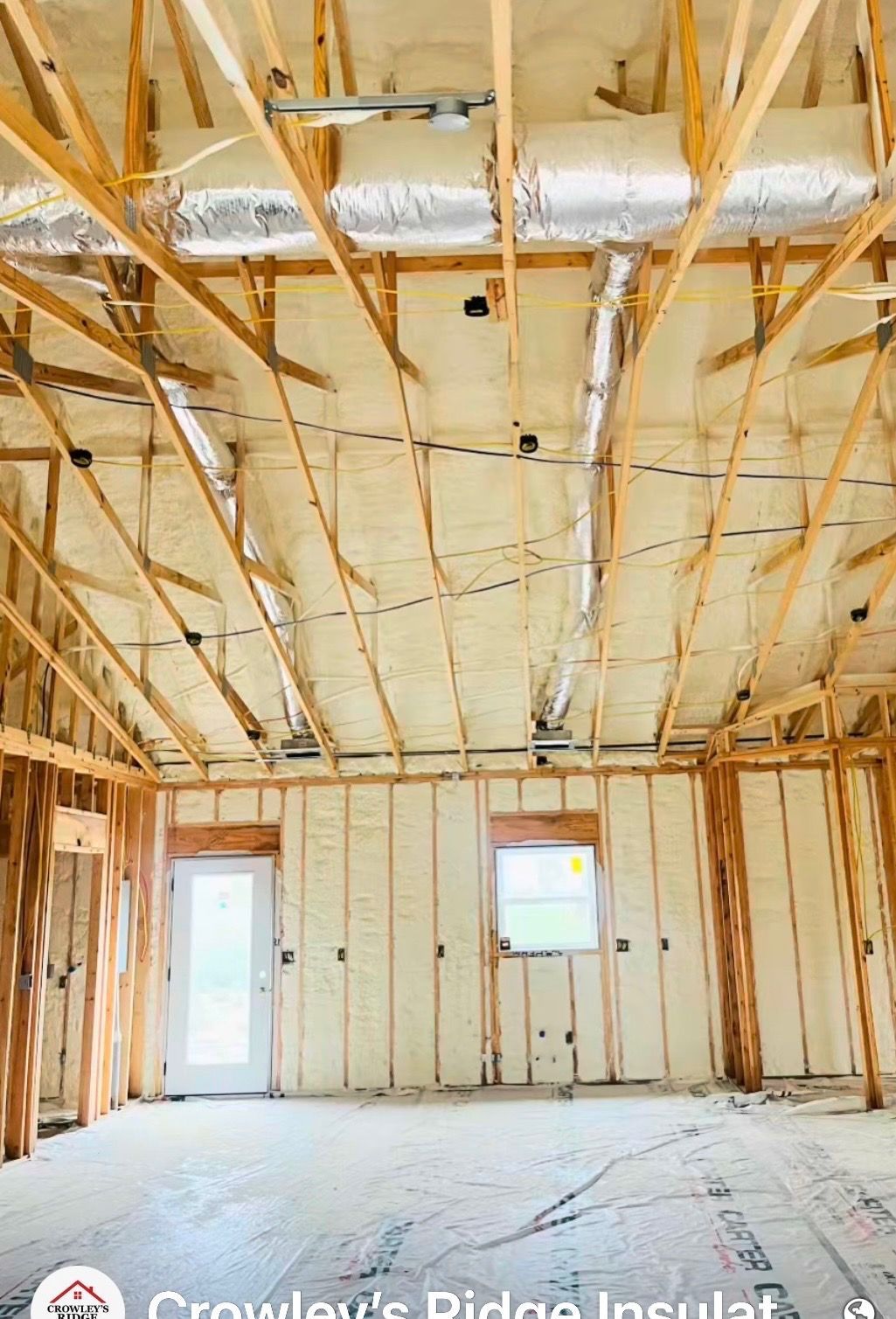 Interior of an unfinished house with exposed insulation, framing, and two windows and a door.