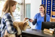 Customer paying at a pet store counter while holding a dog, with a smiling clerk behind the register