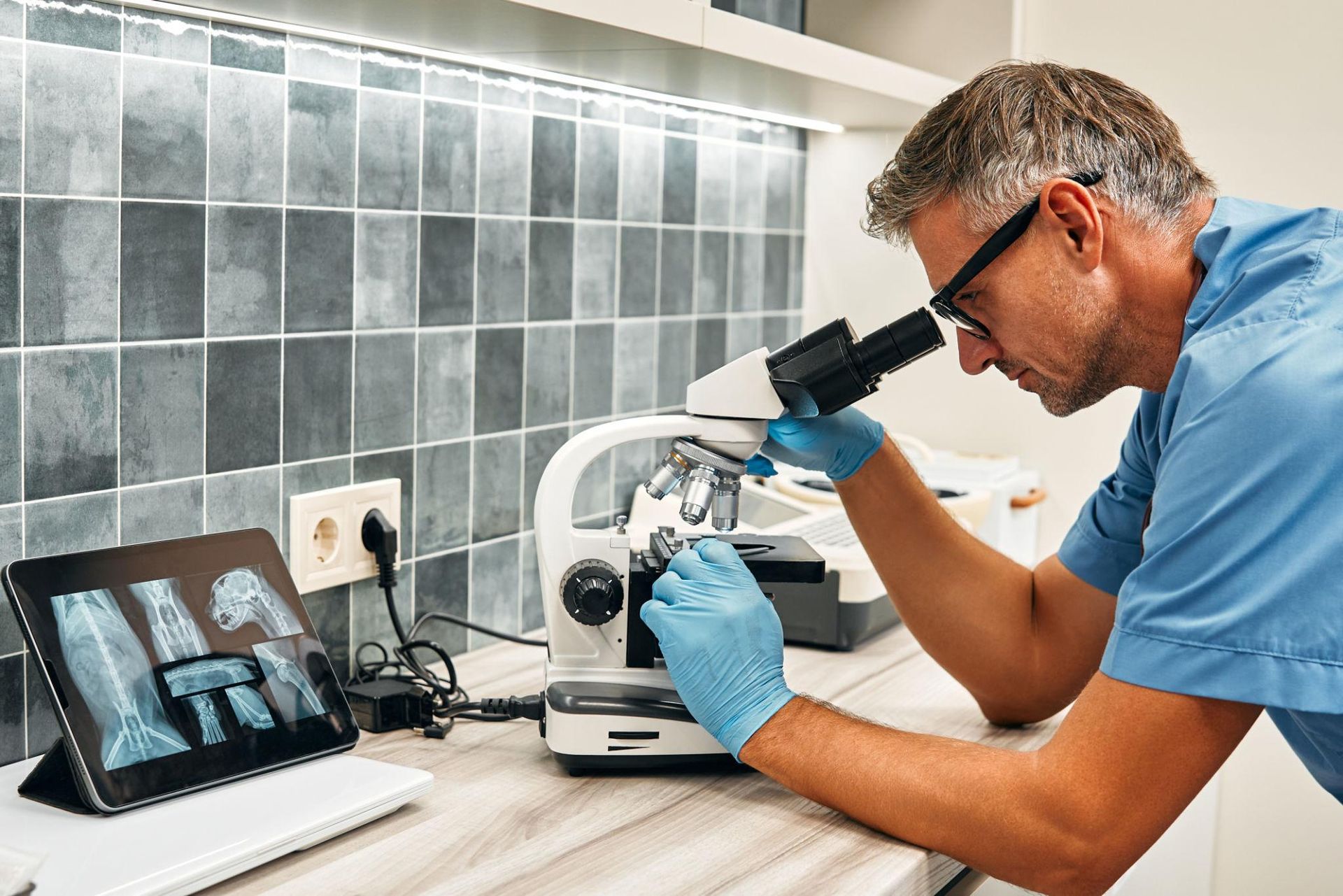 Scientist examining a sample under a microscope beside a laptop in a lab workstation