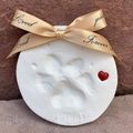 White baby footprint ornament with gold bow and red heart on a brown background