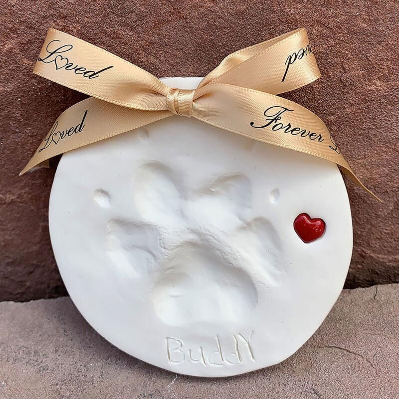White baby footprint ornament with gold bow and red heart on a brown background