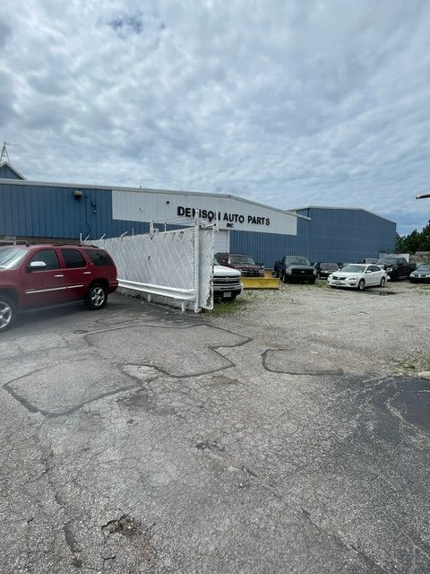 A red SUV parked in front of an auto parts store with a white fence and a partially cloudy sky.