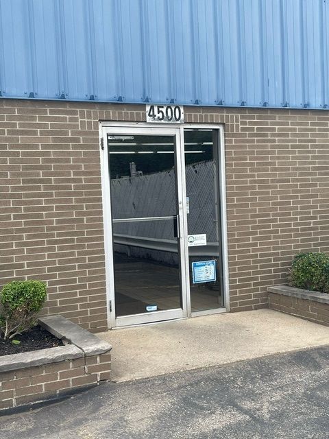 A glass door with the number 4500 above it, set in a brown brick wall beneath a blue corrugated metal roof.