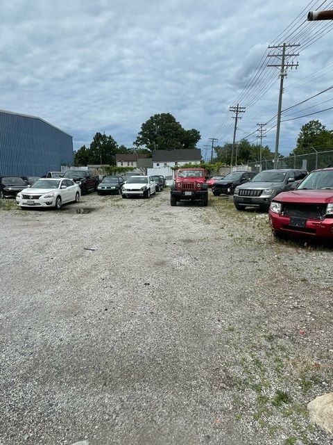 A gravel parking lot filled with several parked vehicles under a cloudy sky.
