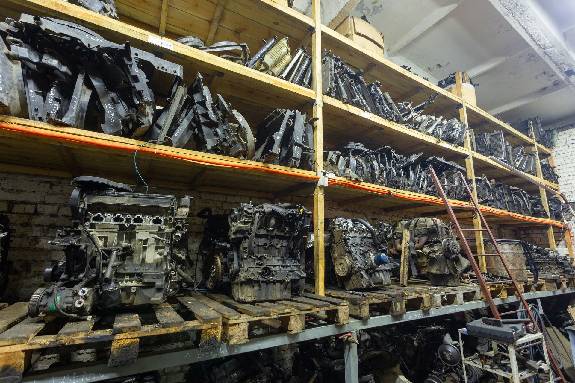 A warehouse interior featuring rows of car engines and parts stacked on wooden pallets and metal shelving units. A warehouse interior featuring rows of car engines and parts stacked on wooden pallets and metal shelving units.