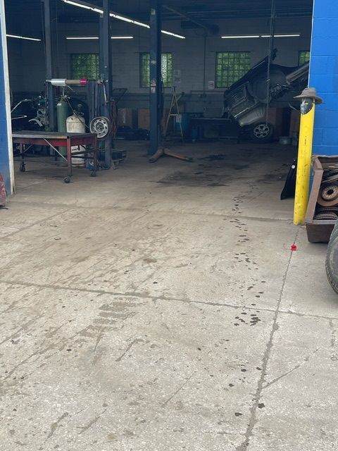 A dimly lit auto repair shop interior featuring concrete floors, a work table, and a car raised on a hydraulic lift.