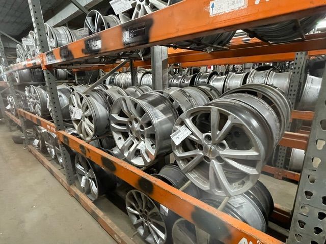 Rows of various silver alloy car wheels are stacked on metal warehouse storage racks.